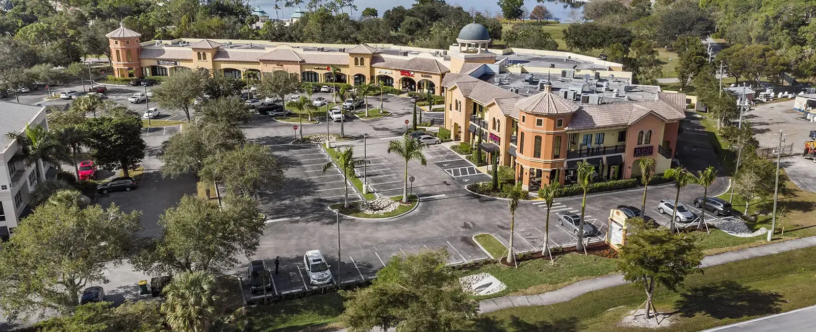 Aerial view of Sugden Park Plaza in Naples, Florida, showing the commercial center, surrounding parking areas, landscaping, access roads, and neighboring properties.
