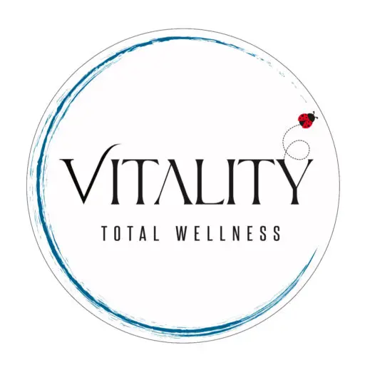 Vitality Total Wellness logo featuring elegant black typography centered within a circular blue brushstroke design, accented by a small red ladybug symbol representing wellness, balance, and personal growth.